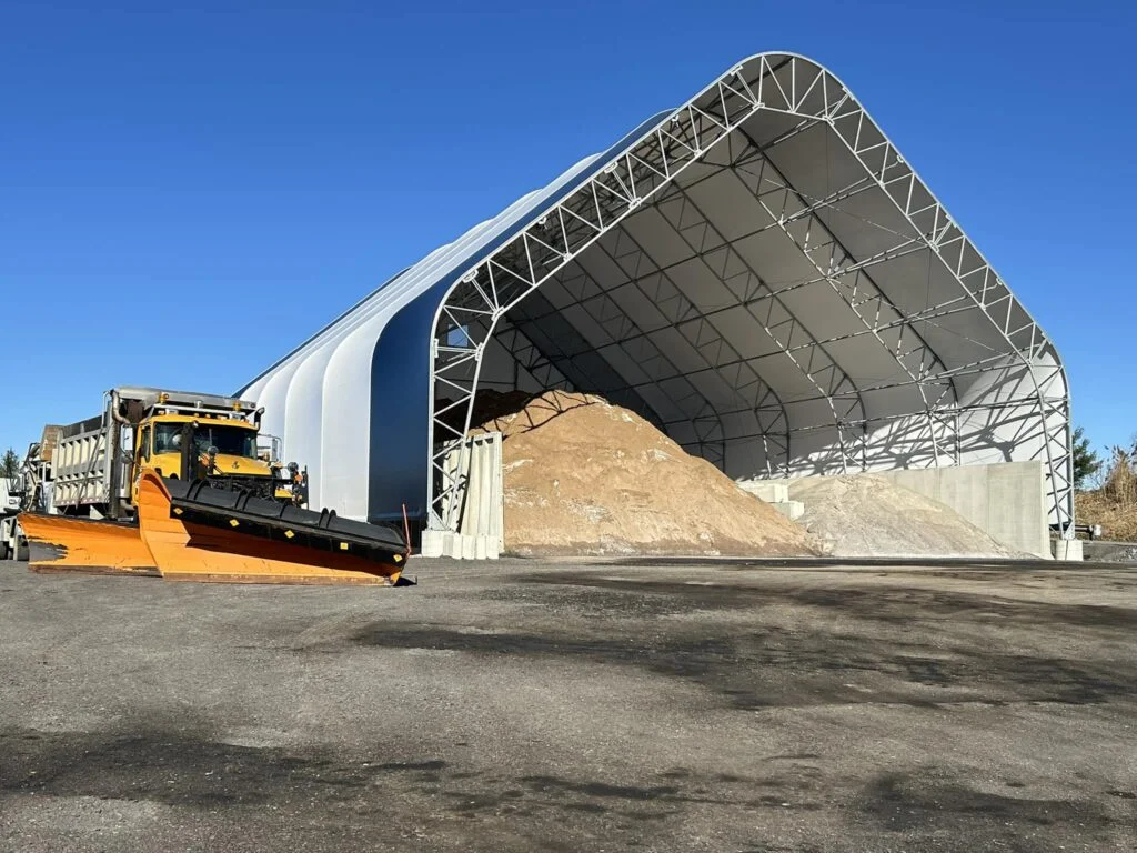Britespan wide-span fabric building used for sand and salt storage with open-front access and a snow plow truck parked outside