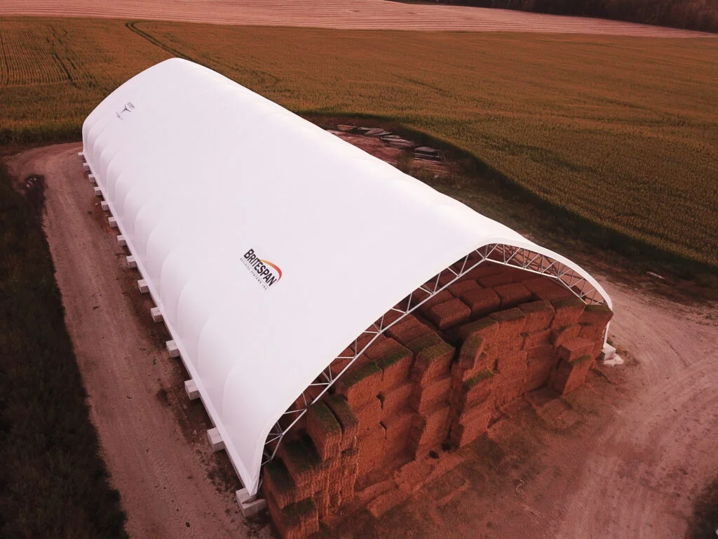 Aerial view of a Britespan Triumph Series arch-style fabric building covering a large stack of hay bales on a farm