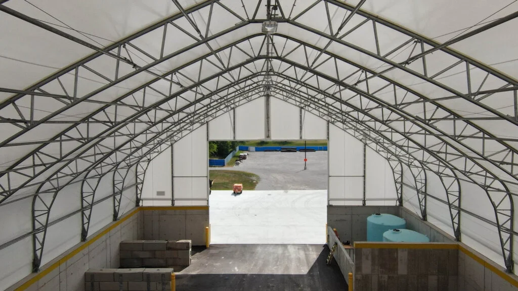 Commercial Fabric Building Interior: Permits and Structures - Britespan Interior view of a large, white fabric building showing its metal truss structure and concrete bins, with an opening leading to an outdoor yard. This commercial fabric structure highlights the type of industrial building that often requires specific fabric building permits.