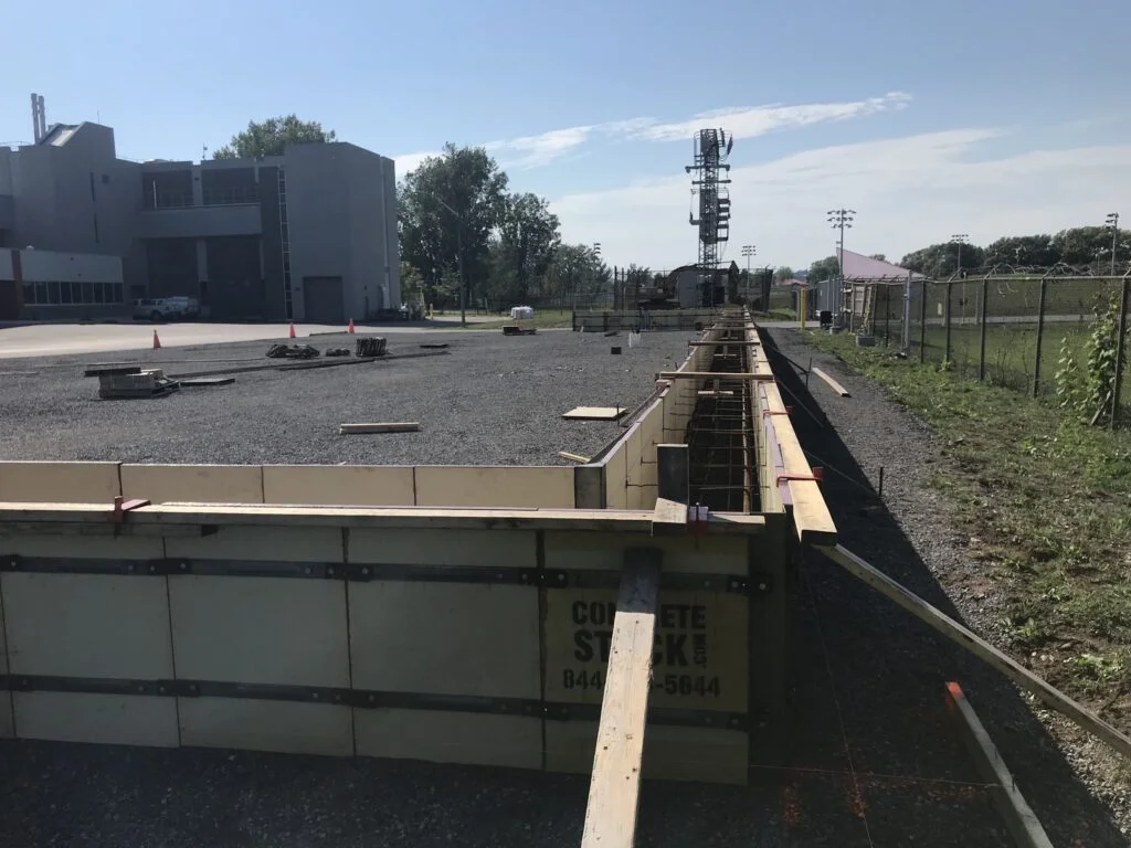 Fabric Building Foundations: Grade Beam Construction - Britespan Long concrete formwork with rebar prepared for a durable fabric building foundation on a construction site, ready for pouring.