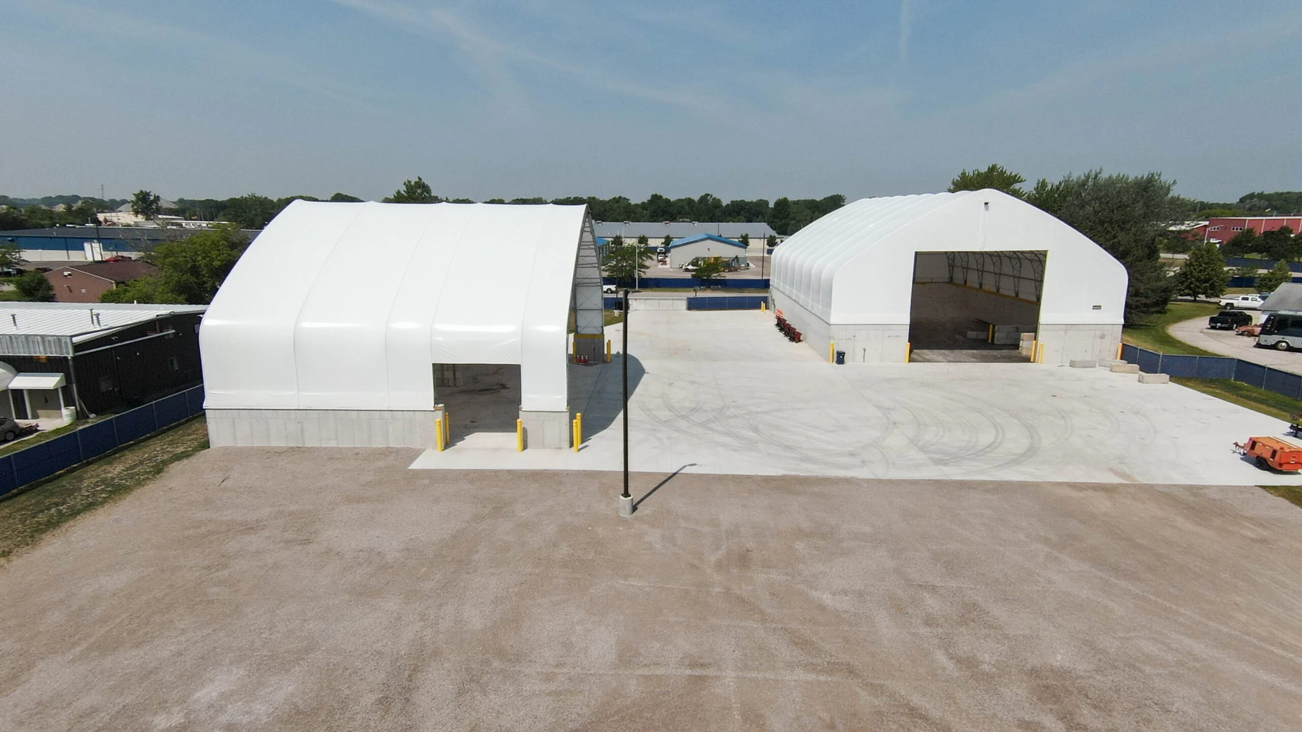 Two large white tension fabric buildings with arching roofs stand on concrete foundations, showcasing durable construction built for a long lifespan.