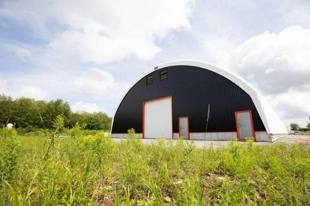 - Britespan Exterior view of a large fabric building with a dark end wall behind a field. It is a clear span fabric distribution centre in the shape of a hoop.