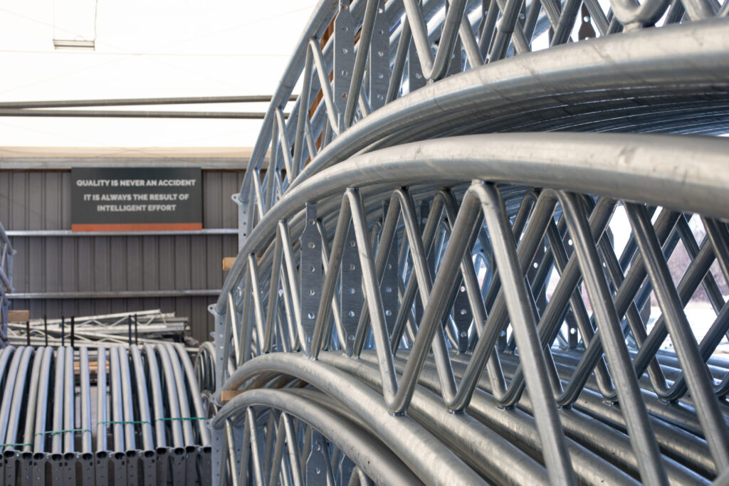 Galvanized steel frame trusses for fabric buildings stacked at Britespan distribution facility. PE Pipe vs Steel Frame Fabric Buildings: What Buyers Should Know Before Building