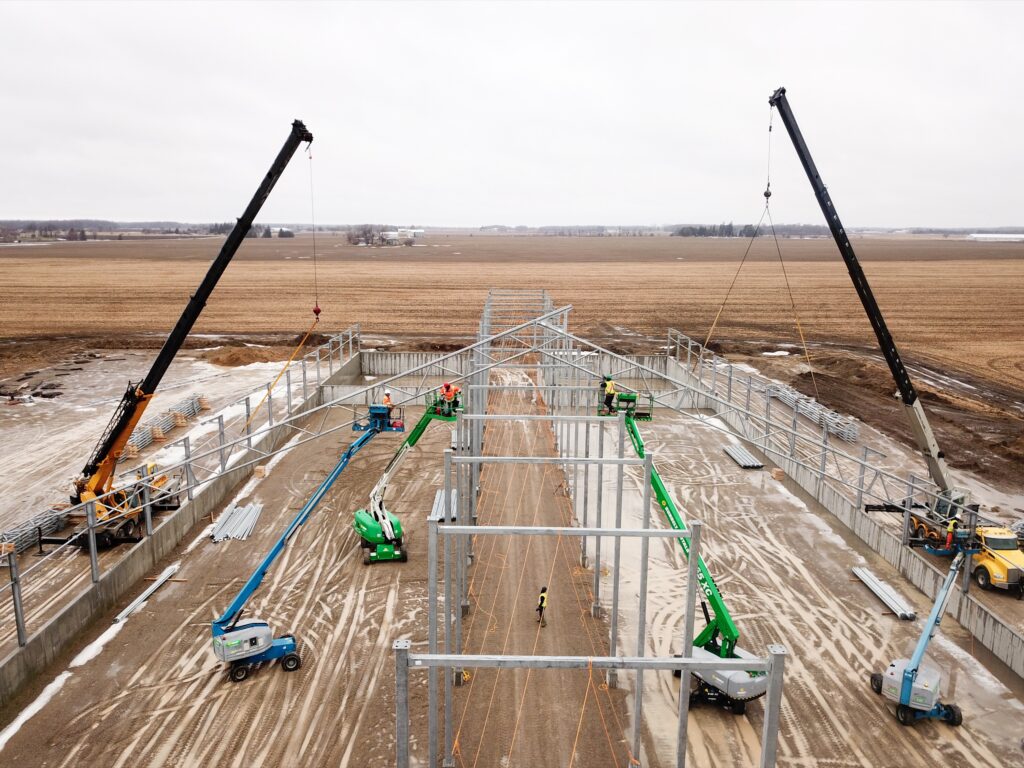 Aerial view of steel frame fabric building construction with cranes erecting trusses at Rasenberg Farms. PE Pipe vs Steel Frame Fabric Buildings: What Buyers Should Know Before Building