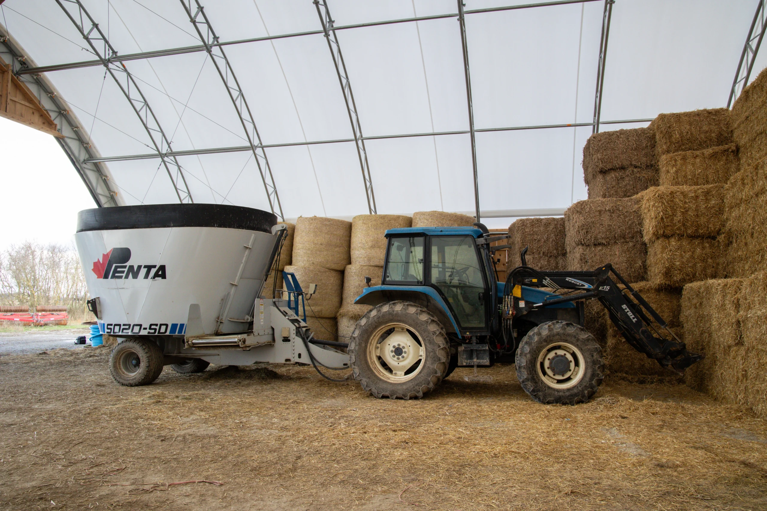 Interior of an Apex fabric building used for combined hay and equipment storage with a tractor and feed mixer
