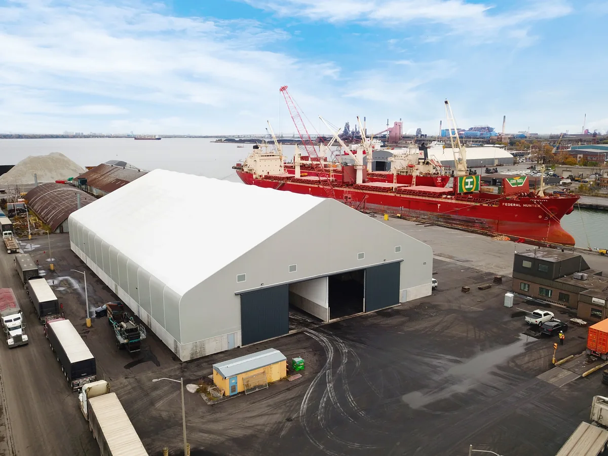 - Britespan Large white fabric hangar at a harbor with a red cargo ship and cranes in the background.